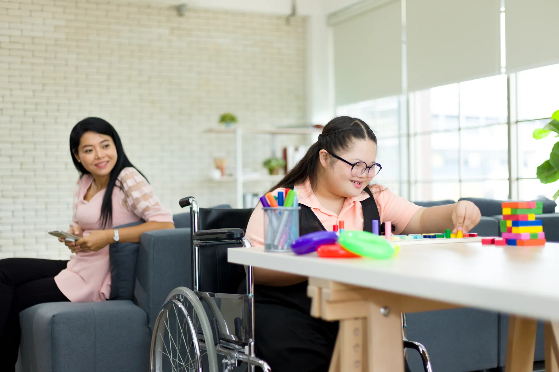 Una chica en silla de ruedas juega con piezas de colores en la mesa del salón