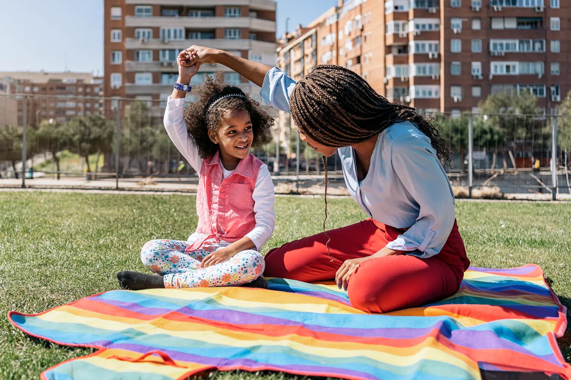 Una cuidadora balla amb una nena asseguda sobre una manta a la gespa d'un parc