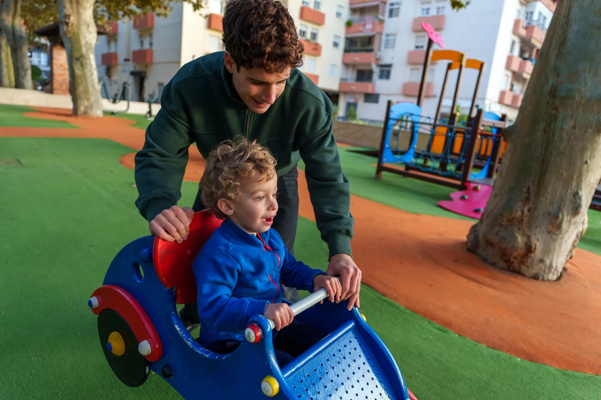 Un germà gran empeny un nen petit en un balancí del parc