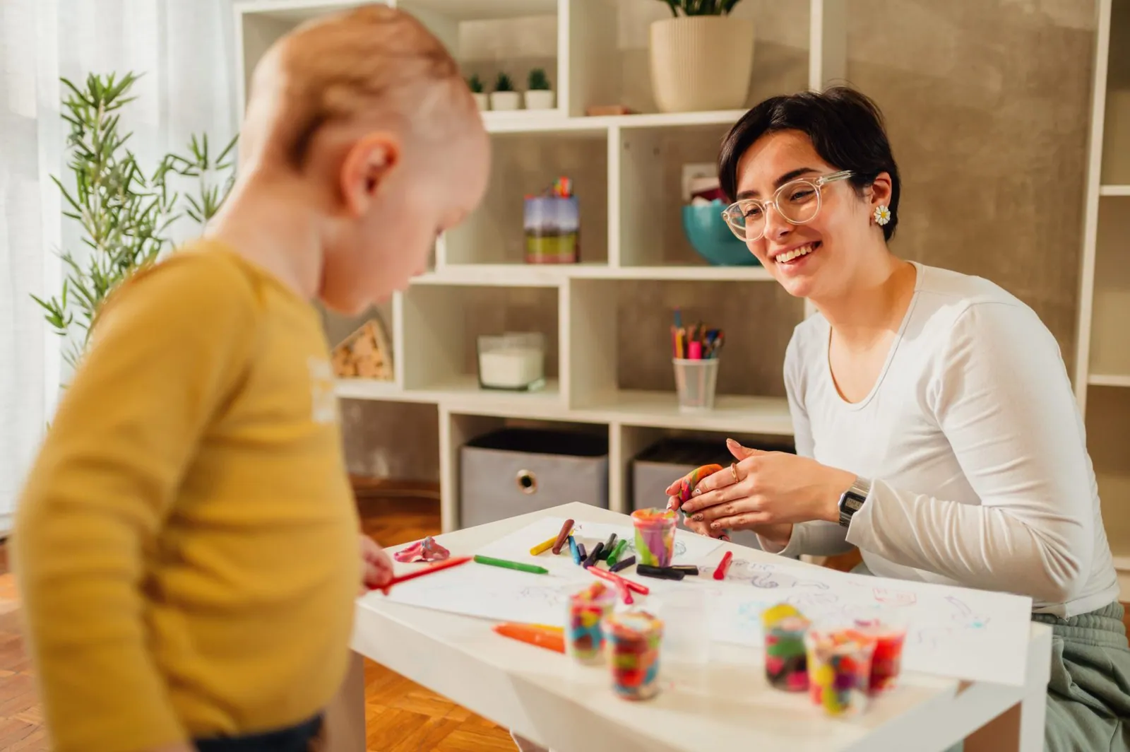 Una cuidadora dibuja con ceras de colores junto a un niño en el salón de casa