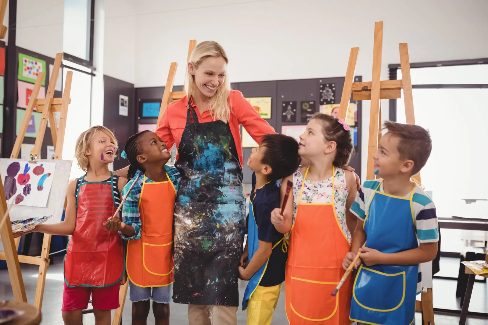 Un grupo de niños con bata ríe en el aula junto a su educadora